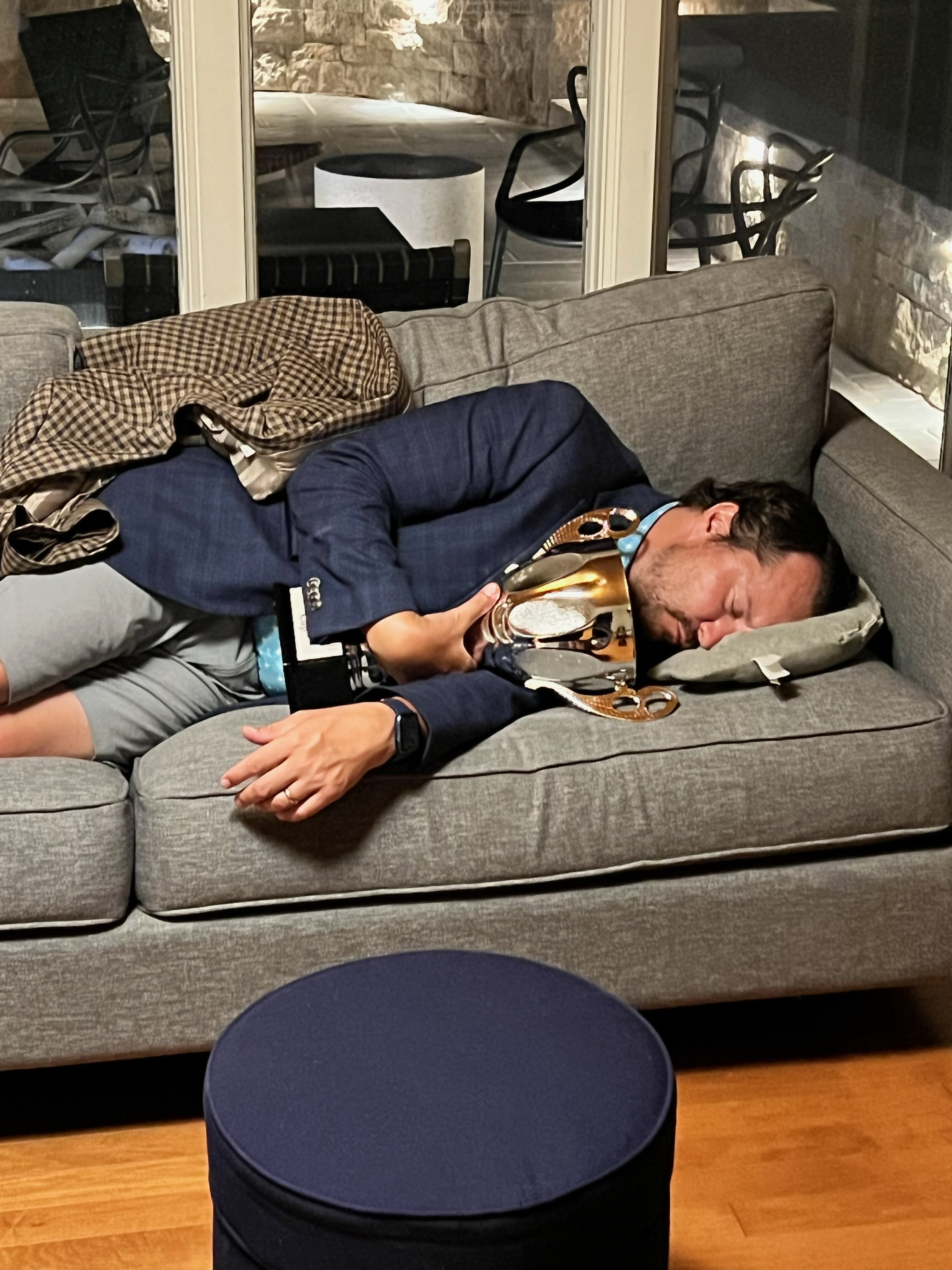 Joe Johns asleep on a sofa while holding the RidgeMawr Cup trophy after the inaugural event